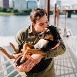 man in brown jacket hugging black and brown short coated dog